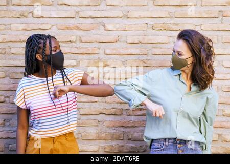 Multiethnische junge Frauen tragen Masken Gruß an einander mit Ihre Ellbogen Stockfoto