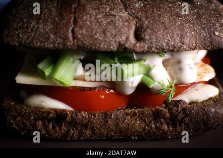Club Sandwich mit Schinken, Käse, roten Tomaten, grünen Zwiebeln Nahaufnahme auf schwarzem Hintergrund. Stockfoto