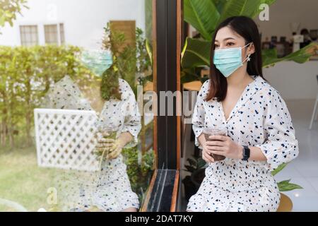 Junge Frau trägt Gesichtsmaske zum Schutz Coronavirus (covid-19) und Trinken Schokoladenmilch im Café Stockfoto