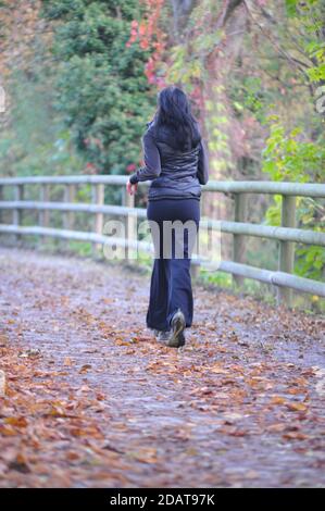 Weibliche Läuferin in schwarz gekleidet, Joggen auf Laub bedeckten Weg im Wald im Herbst Stockfoto