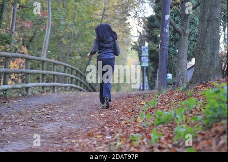 Weibliche Läuferin in schwarz gekleidet, Joggen auf Laub bedeckten Weg im Wald im Herbst Stockfoto