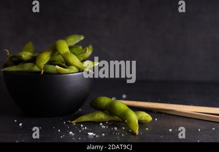 Japanische Vorspeise Edamame grüne Sojabohnen gewürzt mit Salz in einer Schüssel, mit Shop-Sticks auf der Seite. Stockfoto