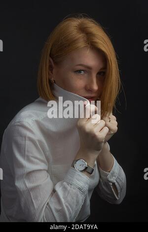 Rothaarige junge Frau mit Sommersprossen, versteckt hinter dem Kragen eines weißen Hemdes Stockfoto