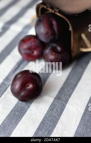 Reife große Pflaumen verstreut auf einer gestreiften Tischdecke aus einem Holzkiste Stockfoto