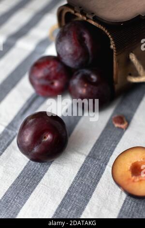 Reife große Pflaumen auf einer gestreiften Tischdecke verstreut und gehackt Pflaumen aus einer Holzkiste Stockfoto