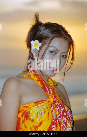 Porträt der jungen indonesierin Frau mit Blume im Haar und Tragen Sarong steht bei Sonnenuntergang 2002 kuta bali indonesia Stockfoto