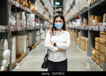 Frau mit medizinischer Maske mit gekreuzten Armen im Lagerhaus während einer Coronavirus-Pandemie (covid-19). Stockfoto