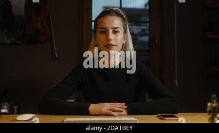 Glückliche blonde Geschäftsfrau am Schreibtisch, Hände auf dem Tisch, mit Video-Gespräch auf Web-Kamera Stockfoto