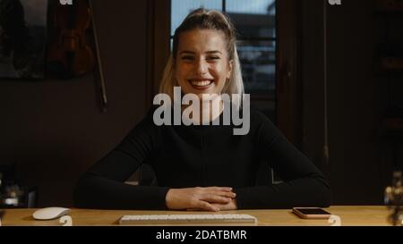 Glückliche blonde Geschäftsfrau am Schreibtisch, Hände auf dem Tisch, mit Video-Gespräch auf Web-Kamera Stockfoto