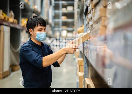 Arbeiter mit medizinischer Maske, der den Bestand im Lager kontrolliert Während einer Coronavirus-Pandemie (covid-19) Stockfoto