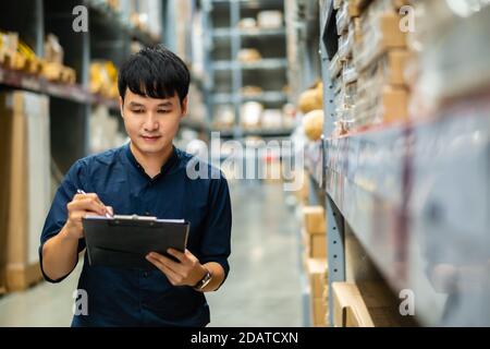 Junger Mann Arbeiter hält Zwischenablage und Überprüfung Inventar in der Lagerhaus Stockfoto