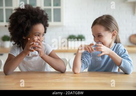 Nette lächelnde verschiedene kleine Mädchen trinken frisches Wasser in der Küche Stockfoto