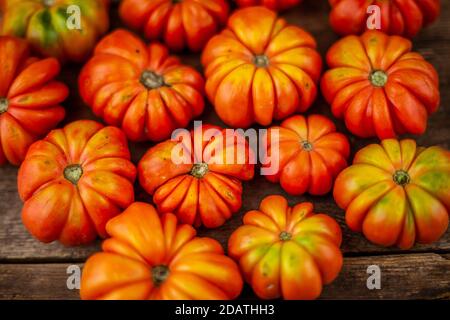 Rote gerippte Tomaten auf einem Holzhintergrund. Amerikanische oder Florentiner Sorte Nina. Das Essen auf dem Tisch war von oben zu sehen. Herbsternte von Gemüse ähnlich Stockfoto