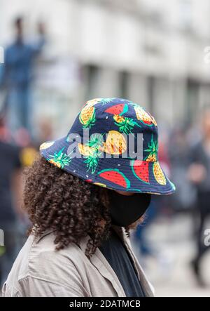 Eine Frau trägt eine Gesichtsmaske und einen farbenfrohen Sonnenhut während eines Protestes zu Black Lives Matter. Stockfoto