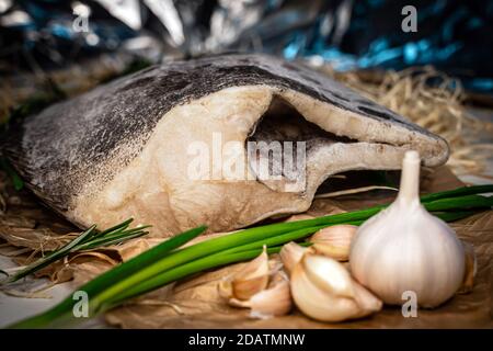 Roher frischer grönländischer Heilbutt ohne Kopf. Fisch mit Knoblauch, Rosmarin und grünen Zwiebeln Stockfoto