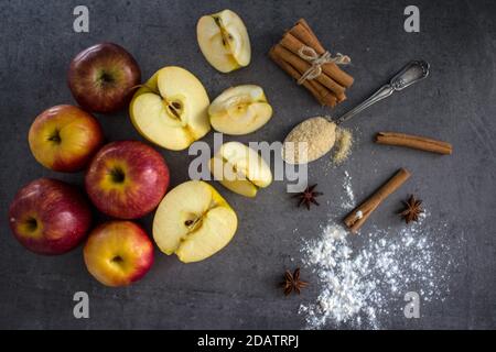 Apfelkuchen vorbereiten. Frische Äpfel, Teig in Backform, Zimtstangen, Zucker und Mehl auf einem Tisch. Stockfoto