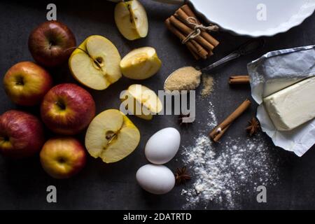 Apfelkuchen vorbereiten. Frische Äpfel, Teig in Backform, Zimtstangen, Zucker und Mehl auf einem Tisch. Stockfoto