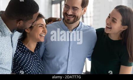 Glückliche, multiethnische Teamkollegen, die sich im Büroflur umarmen und warme Beziehungen demonstrieren Stockfoto