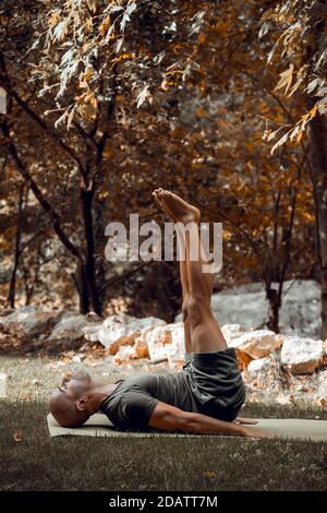 Schöner sportlicher Mann, der Yoga im Herbstpark macht. Athletic Guy Training Im Freien. Genießen Sie Ein Friedliches Workout. Gesunder Lebensstil. Stockfoto