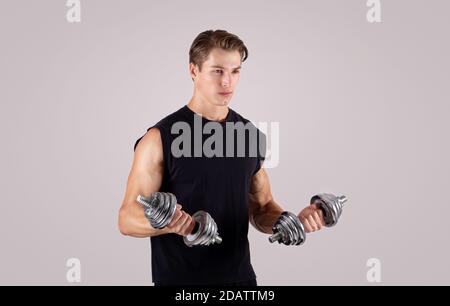 Entschlossener junger Mann, der mit Hanteln über dem Lichtstudio arbeitet Hintergrund Stockfoto