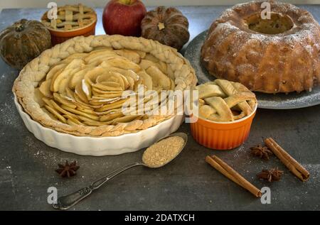 Apfelkuchen verschiedener Art auf einem Tisch mit frischem Obst, Zimtstangen und Kürbissen. Herbstmenü-Ideen. Hausgemachte Dessert Nahaufnahme Foto. Stockfoto