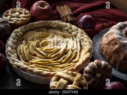 Apfelkuchen verschiedener Art auf einem Tisch mit frischem Obst, Zimtstangen und Kürbissen. Herbstmenü-Ideen. Hausgemachte Dessert Nahaufnahme Foto. Stockfoto