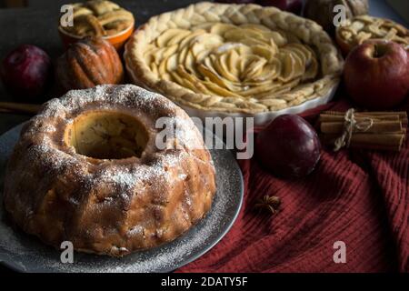 Apfelkuchen verschiedener Art auf einem Tisch mit frischem Obst, Zimtstangen und Kürbissen. Herbstmenü-Ideen. Hausgemachte Dessert Nahaufnahme Foto. Stockfoto