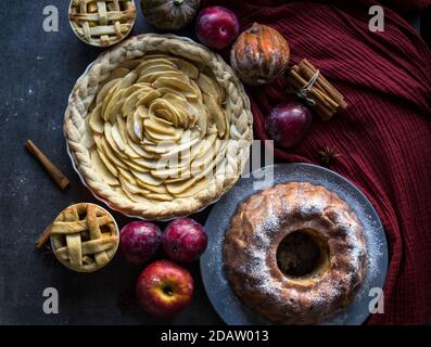 Desserttörtchen auf einem Tisch. Foto von oben mit verschiedenen Apfelkuchen, Kuchen und Torten, frischen Pflaumen, Äpfeln und Kürbissen. Herbstmenü-Ideen. Stockfoto
