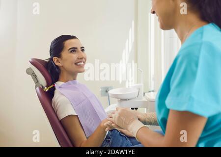 Zahnärztlicher Spezialist hält Hand der glücklichen Frau im Stuhl sitzen In der Zahnarztpraxis Stockfoto