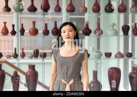 Eine chinesische Frau, die in der Nähe eines Regals verschiedener Vasen im walters Kunstmuseum in baltimore maryland steht. Stockfoto