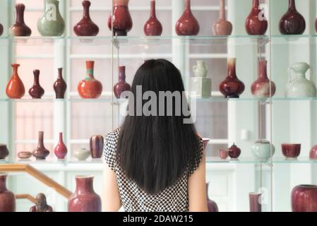 Eine chinesin, die ein Regal mit verschiedenen Vasen im walters Kunstmuseum in baltimore maryland betrachtet. Stockfoto