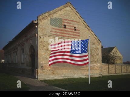 Die Flagge der Vereinigten Staaten von Amerika flattert vor einem alten Bauernhaus, die Flagge der Vereinigten Staaten grunge an der Wand. Stockfoto