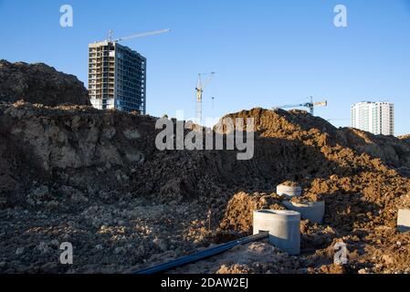 Turmdrehkrane arbeiten auf der Baustelle gegen grauen Himmel. Verlegung von Betonschächten und Abflussrohren für das Regenwassersystem. Bau Regenwasser und U Stockfoto