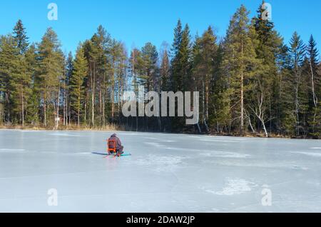 Älterer Mann sitzt allein auf Kicksled und Eisfischen auf gefrorenem See im Winter, Finnland Stockfoto