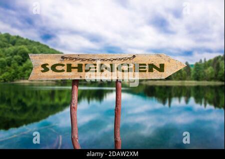 Schengen Holzpfeil Straßenschild gegen See und Wald Hintergrund. Schengen - Europäischer Grenzkontrollraum Stockfoto