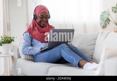 Genießen Sie die Zeit zu Hause. Schwarze muslimische Frau mit Laptop und Kaffee trinken Stockfoto