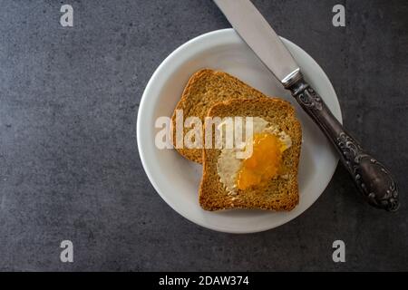 Foto von oben von Toasts mit Butter und Marmelade auf weißem Teller. Dunkelgrauer strukturierter Hintergrund. Stockfoto