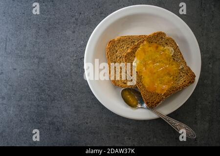 Foto von oben von Toasts mit Butter und Marmelade auf weißem Teller. Dunkelgrauer strukturierter Hintergrund. Stockfoto