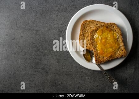 Foto von oben von Toasts mit Butter und Marmelade auf weißem Teller. Dunkelgrauer strukturierter Hintergrund. Stockfoto