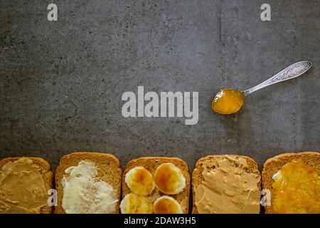 Rahmen oder Rahmen aus Toastbrot mit verschiedenen Belägen. Süßes Frühstück Draufsicht Foto. Dunkelgrauer strukturierter Hintergrund mit Kopierbereich. Stockfoto