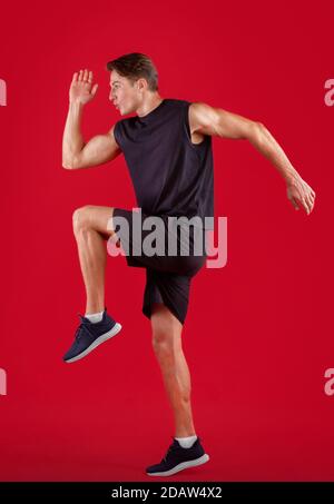 Seitenansicht des jungen männlichen Sprinters laufen, Training auf rotem Studio-Hintergrund Stockfoto