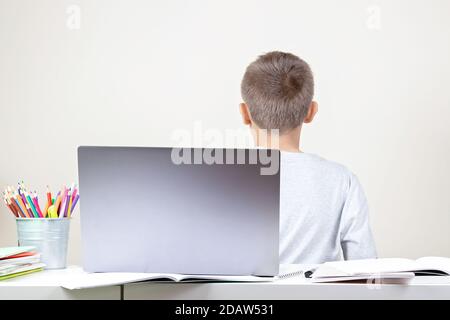 Online-Bildung, Lernschwierigkeiten. Der Junge, der am Schreibtisch sitzt, dreht sich mit einem Laptop und einem Haufen Schulbücher um Stockfoto