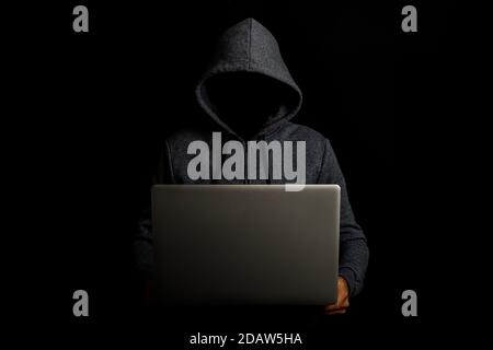 Mann ohne Gesicht in einer Kapuze hält einen Laptop auf einem dunklen Hintergrund. Konzept von Cyber-Rogue, Hacker. Banner. Stockfoto