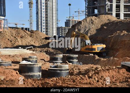 Bagger auf Erdarbeiten während der Verlegung der Rohre der Heizungsanlage zu einem neuen Wohngebäude auf der Baustelle. Verlegung von Betonabwasserkanälen Stockfoto