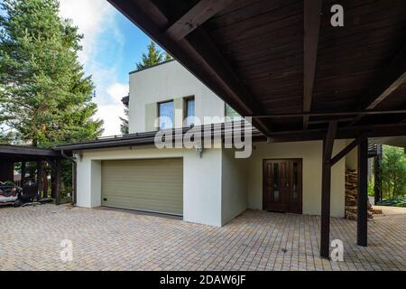 Modernes Äußeres von Luxus-Privathaus mit eingebauter geschlossener Garage. Holzdach. Schließen Sie die Tür. Holzstapel in der Nähe der Wand. Stockfoto