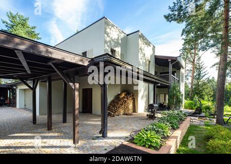 Modernes Äußeres von luxuriösem privaten Cottage. Holzstapel in der Nähe der Wand. Grüner Garten und Terrasse. Grill. Holzdach. Stockfoto