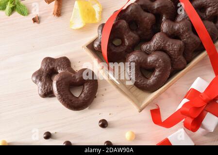 Herz- und sternförmige Schokoladenkekse auf Tablett und Zimtstangen und Zitrone auf Holztisch mit Geschenk. Draufsicht. Horizontale Zusammensetzung. Stockfoto