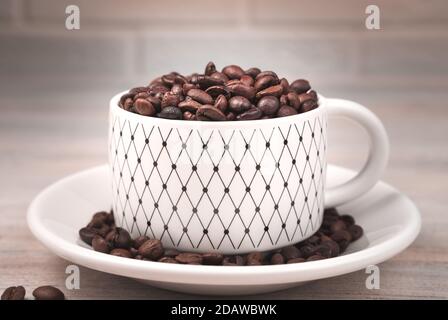 Die weiße Tasse wird mit gerösteten Kaffeebohnen gefüllt. Stockfoto