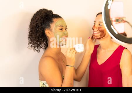 Glücklich lächelnde Familie Anwendung Gesichtskaffee Maske Porträt. Junge Influencer Mädchen mit Hautpflege Cleanser Spa Tag mit Mama. Konzentrieren Sie sich auf kleine Tasse. Stockfoto