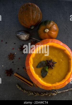 Kürbissuppe in Kürbisschüssel. Draufsicht Foto von Kürbis, Äpfeln, Karotten Anis Sterne und Zimtstangen. Grauer Hintergrund. Herbstfutter Nahaufnahme Foto. Stockfoto